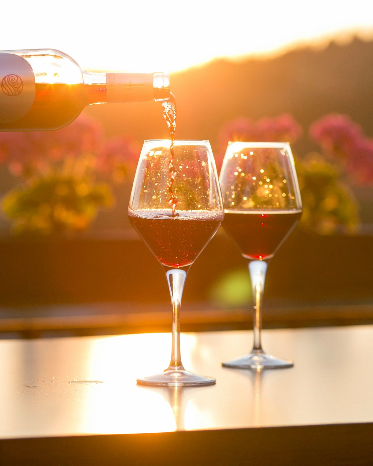 Wine poured into two glasses at golden hour, the Tuscan hills behind